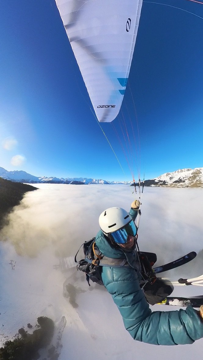 Olly flying with skis on his harness above a winter sea of cloud