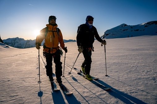 Two ski tourers skinning across a snowfield at sunrise